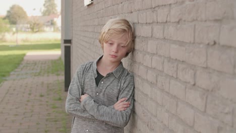 sad, adorable, cute, boy standing alone to the wall with arms crossed, almost crying because he is bullied