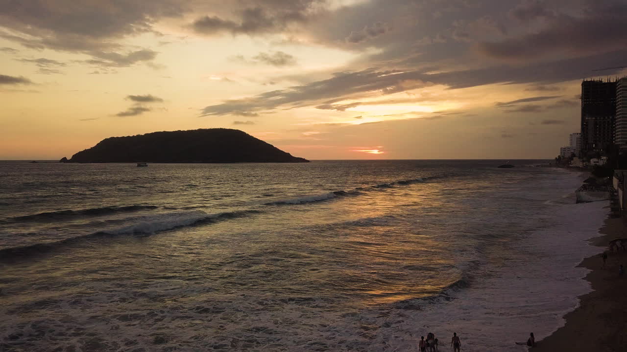 gente irreconocible divirtiéndose en la orilla de la playa en una puesta de sol amarilla