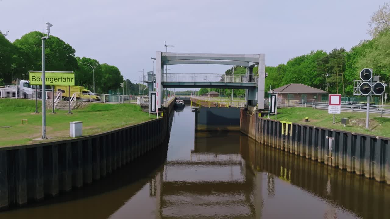 Camera fixed showing mechanical opening of lock gate with reflections on water and trees around, under clear daylight in rural setting.