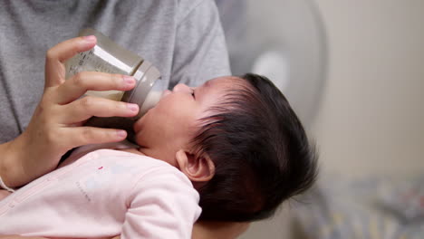 sucking some milk from a baby bottle, a newborn child is falling in and out of sleep as its mother is holding her in her arms