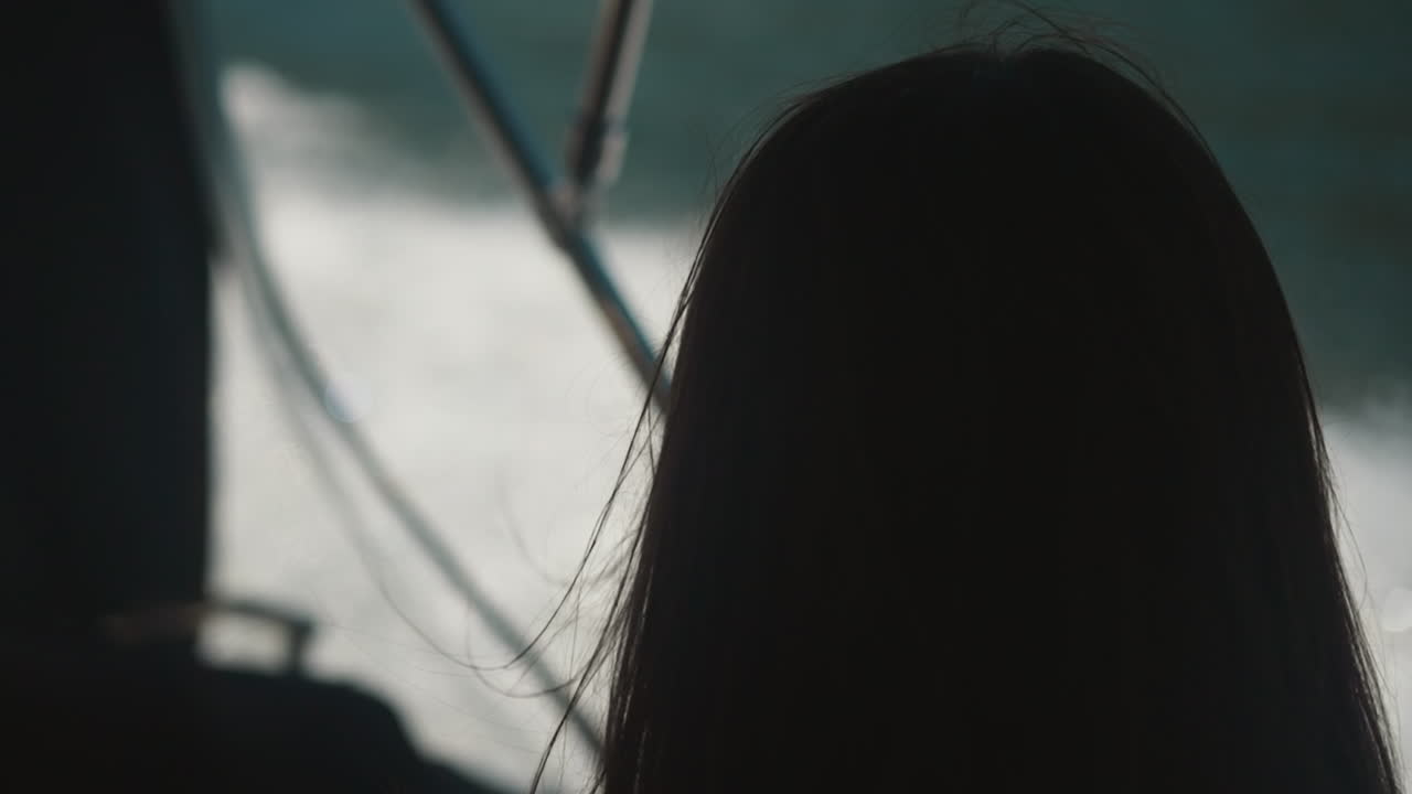Silhouette of long-haired woman on background of blurred foaming water closeup. Calm young lady looks at sea surface thoughtfully standing on boat backside view slow motion