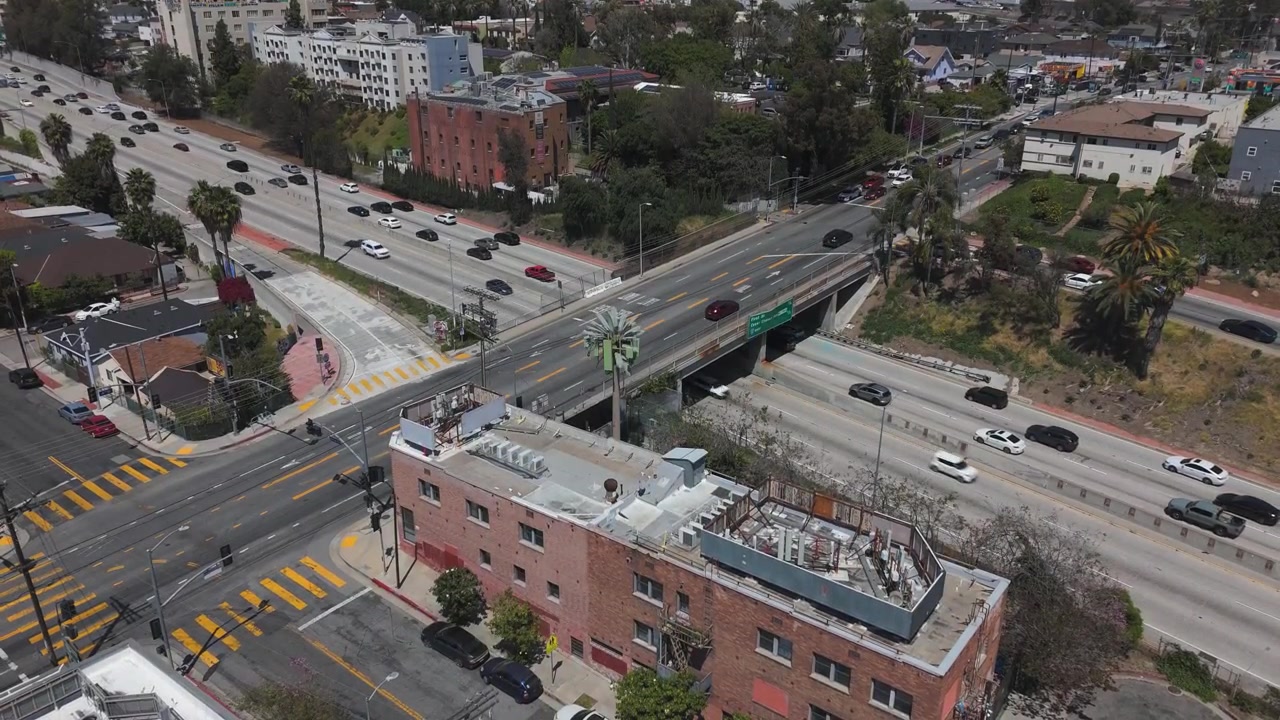 Autopista en Los Ángeles con tráfico. Edificio de ladrillo rojo en primer plano con cielo azul despejado en un día soleado de California. Toma aérea 4K a 60fps
