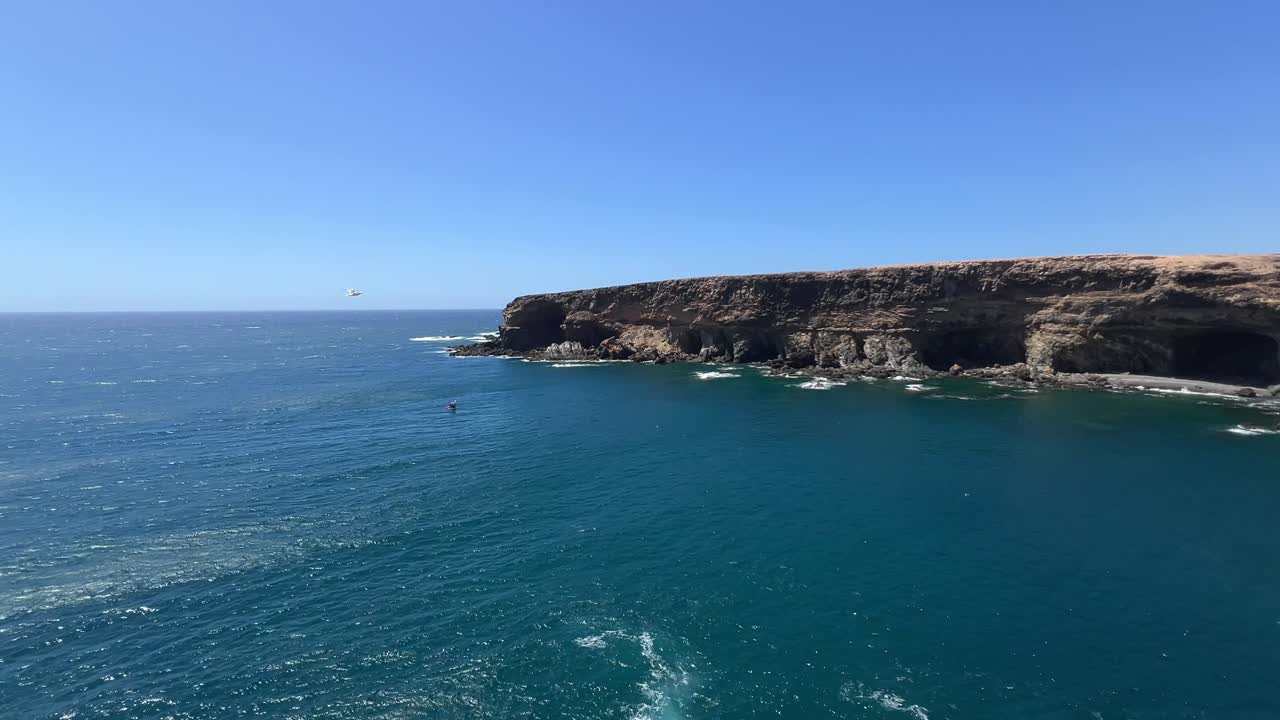 Scenic view of the dramatic volcanic cliffs and sea caves of Ajuy meeting the blue Atlantic Ocean on a sunny day in Fuerteventura, Canary Islands, Spain