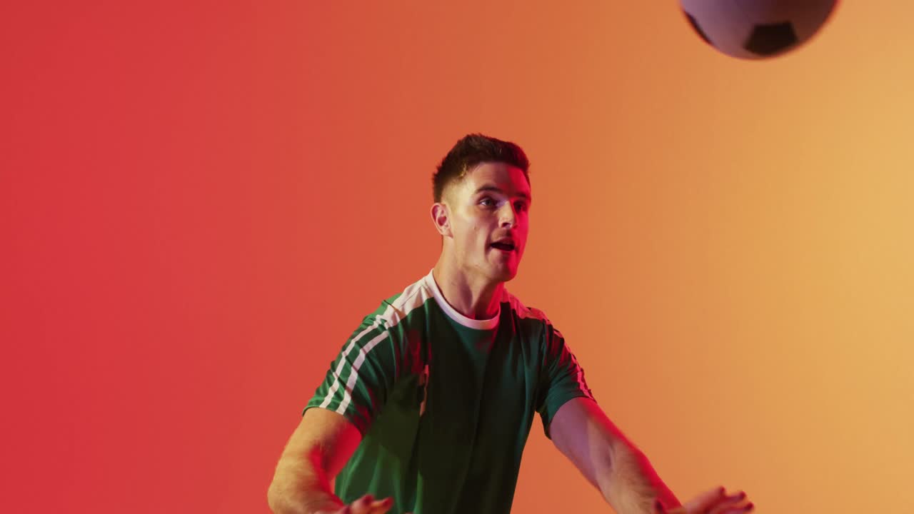Caucasian male soccer player returning football with head over neon pink lighting