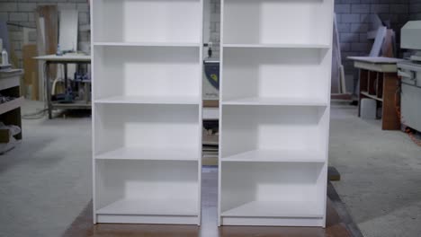 two white finished cupboard with shelves are standing in a workshop of carpentry, vertical panorama