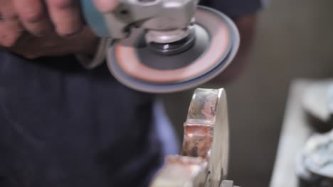 craftsman polishes a violins body using a mechanical hand grinder in a workshop