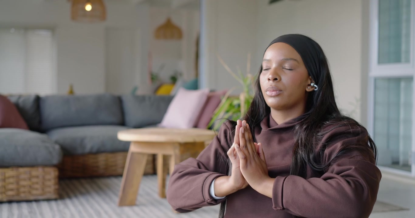 African American adult woman tapping earbud, starting meditation and stretching to prayer at home