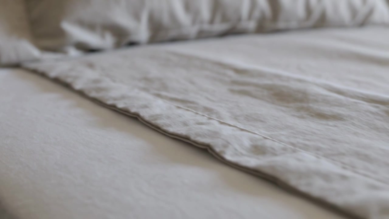 Movimento della telecamera su lenzuolo piegato e cuscino in camera da letto, mostrando le cuciture e la trama del tessuto.