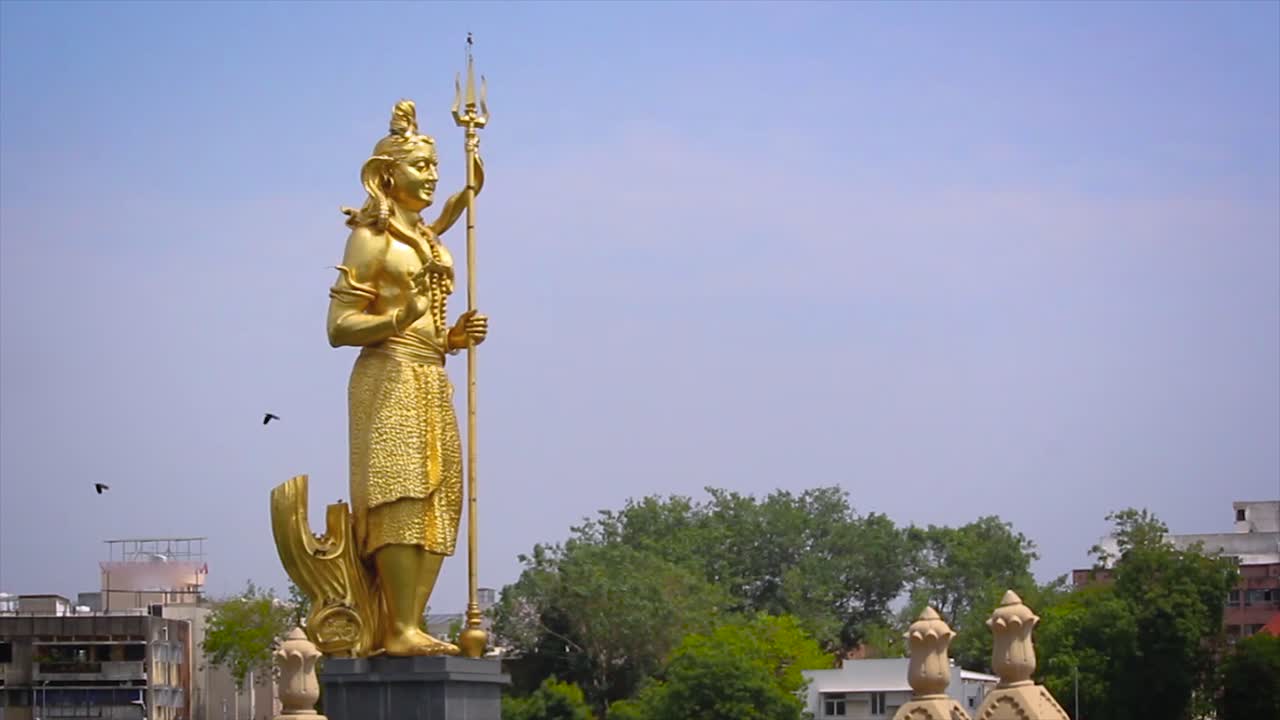 Stunning footage of towering golden statue of Lord Shiva, prominent spiritual and cultural landmark, located in serene Sursagar Lake in Vadodara, Gujarat.
