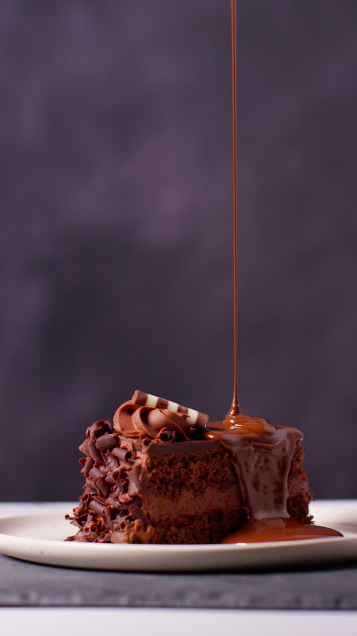 video vertical de una persona vertiendo salsa de chocolate derretido en una rebanada de pastel de chocolate y comiéndola