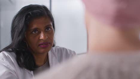 serious female doctor or oncologist giving bad news at meeting with woman patient wearing headscarf undergoing chemotherapy treatment for breast cancer in hospital