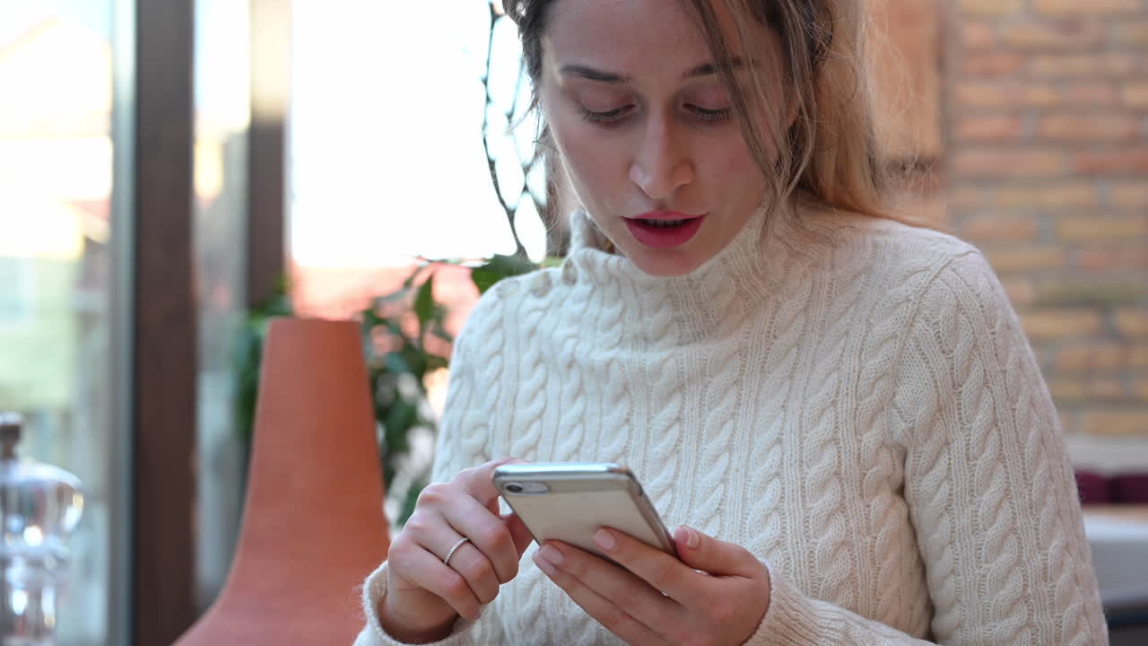 Primo piano di una donna con un dolcevita bianco che scorre lo schermo del telefono in un ristorante