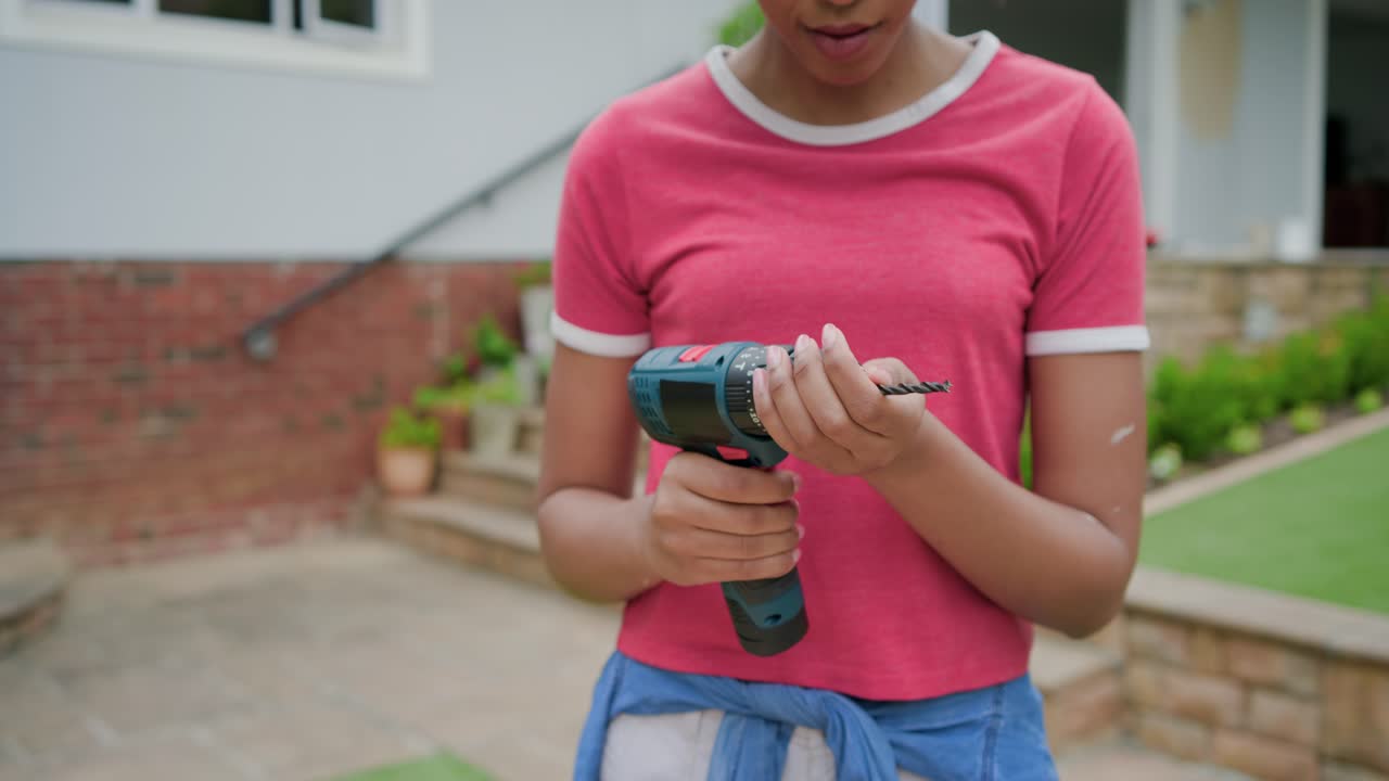 Donna con maglietta rosa che controlla e inserisce una punta in un trapano a batteria, forando un'asse sul patio.