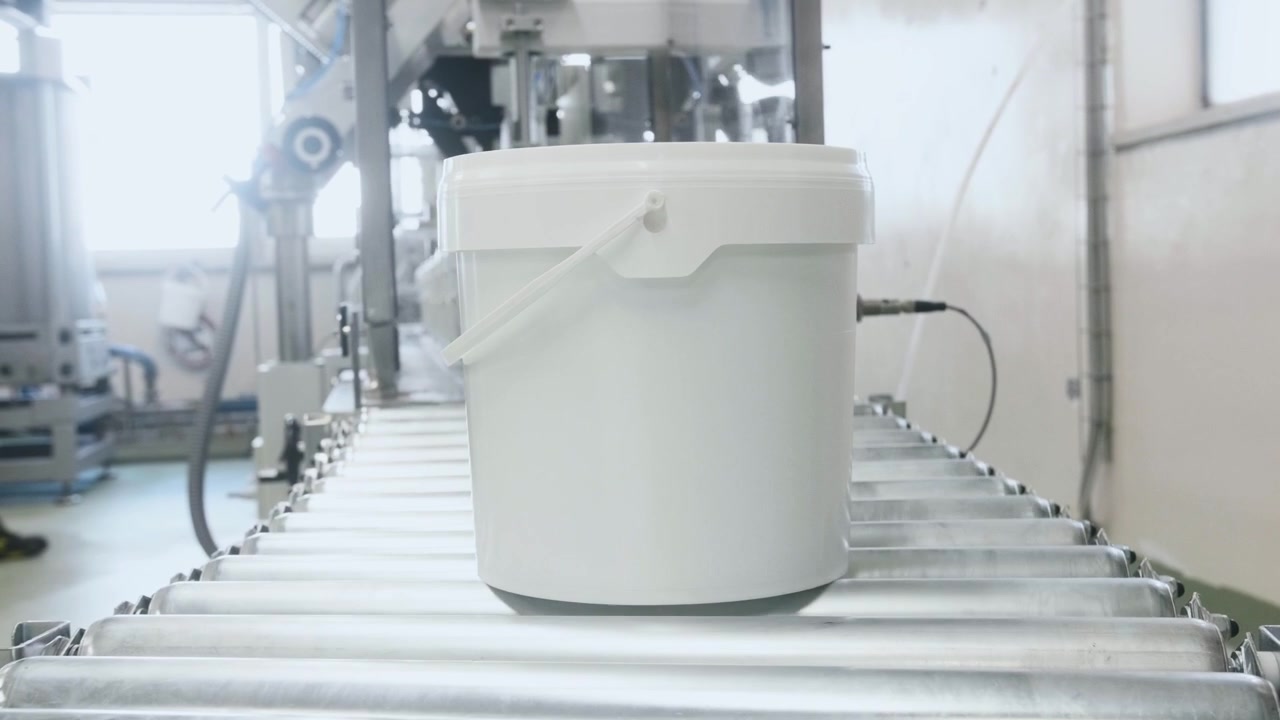 White industrial buckets moving along a conveyor belt inside a modern processing factory, illustrating large-scale automated manufacturing and packaging operations