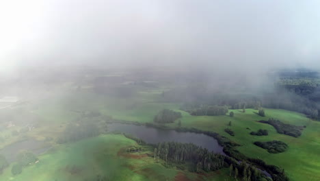 niebla de valle bajo sobre un paisaje verde y exuberante con estanques y bosquecillo de árboles - sobrevuelo aéreo