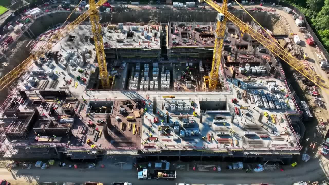 A large construction site showcases cranes and workers busy with building activities. The project involves significant groundwork and structural development in an urban location.