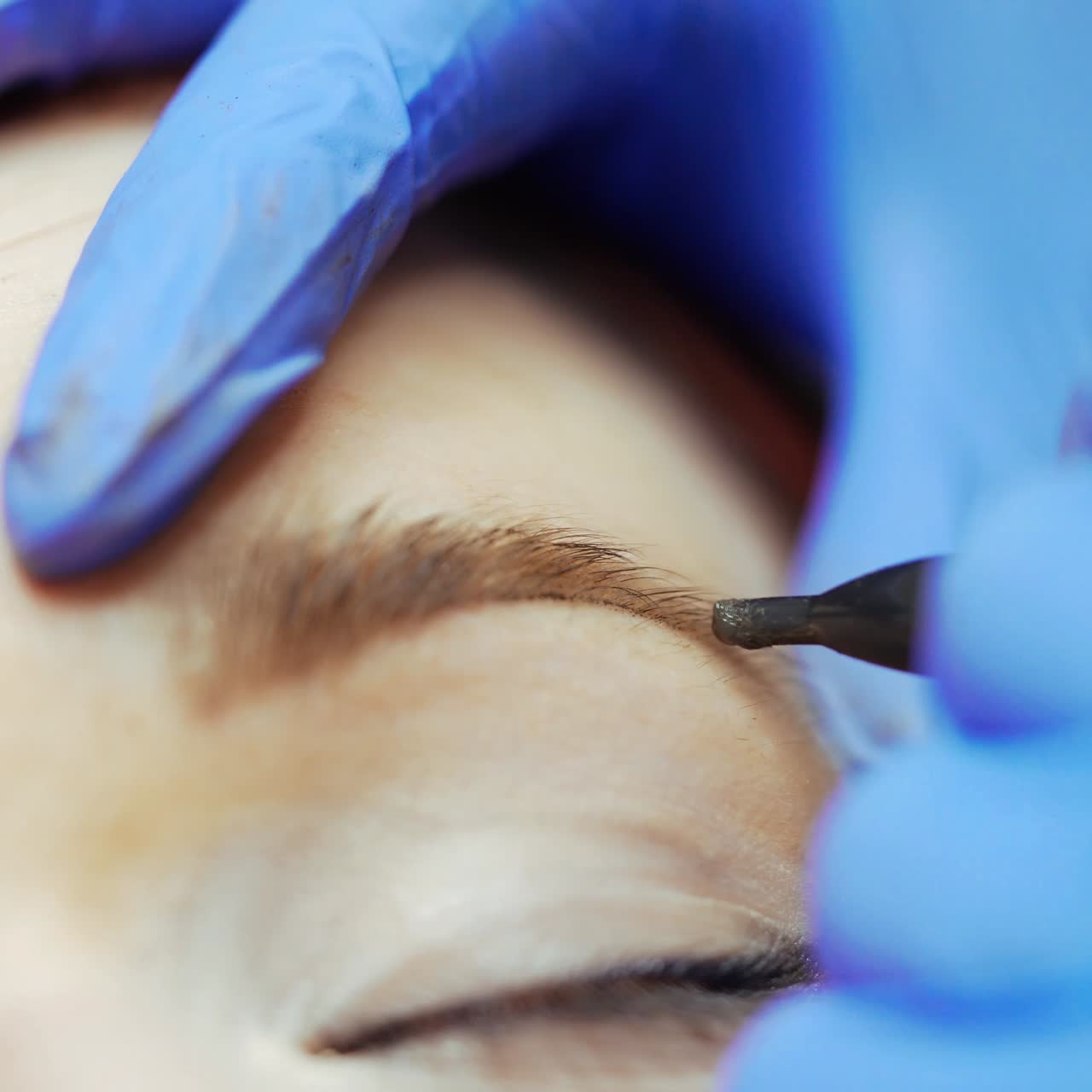 Tattoo specialist in gloves is drawing eyebrows with a thin needle for a woman in a beauty salon. Close-up