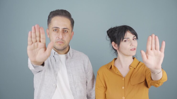 Couple looking at camera and making stop sign.