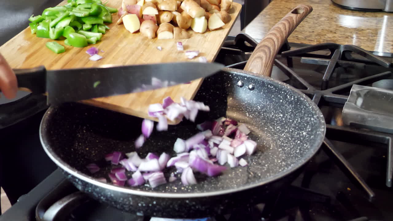 Pushing red onions and peppers into hot pan to cook, potatoes on wooden cutting board