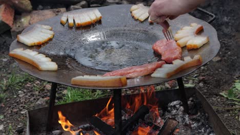 person places meat on grilling disc with hungarian pork fat, szalonna, cooking over fire