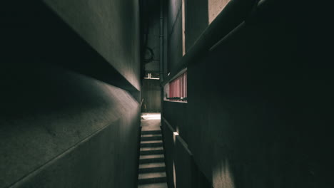 a dark and narrow alleyway with concrete walls and stairs leading up.