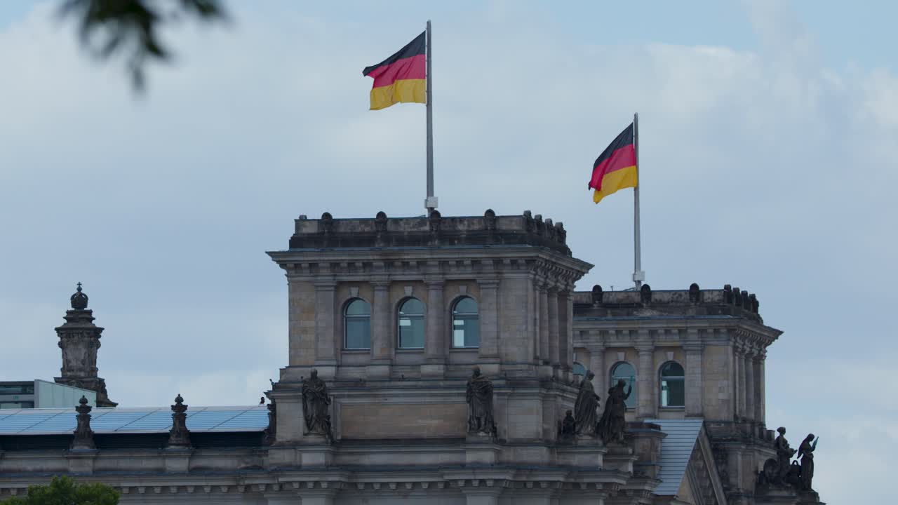 German flags wave atop historic architecture under cloudy sky, static camera, soft daylight, Berlin