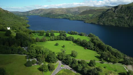 lush green wooded countryside with winding road, dark lake surrounded by mountains and cloud shadows moving across landscape