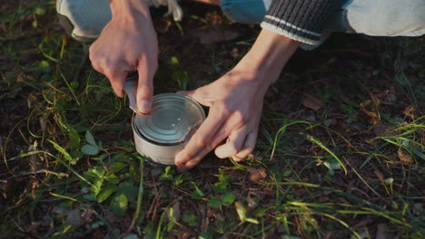 close up fair skin person opening can food seated crossed leg outdoor camping forest nature travel leisure adventure survival cooking picnic young casual lifestyle journey environment