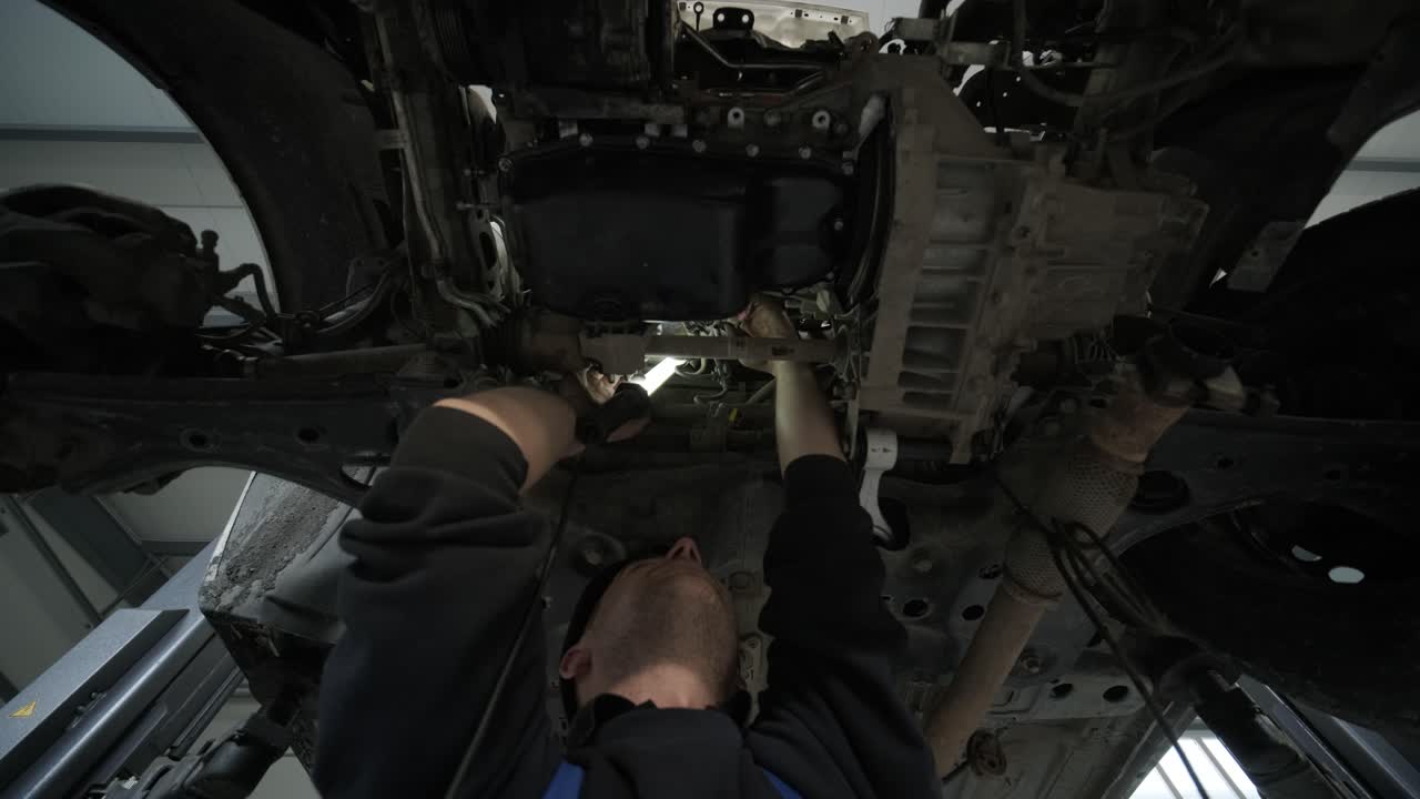 Auto mechanic working underneath car lifting machine at the garage. Auto repair shop. Car service, repair.