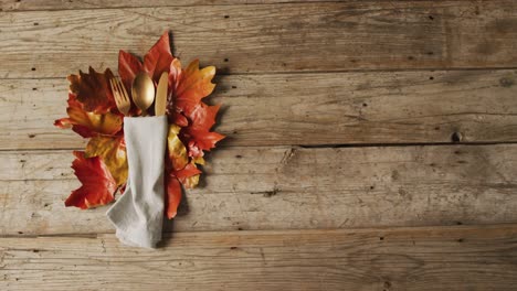 Video-of-cutlery,-cloth-and-autumn-decoration-with-leaves-lying-on-wooden-surface