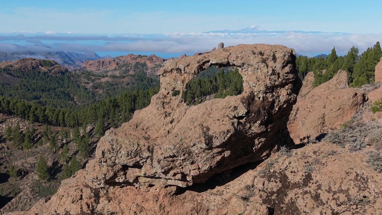 Ripresa aerea orbitale attorno all'arco di pietra di Ventana del Nublo a Gañifa, che rivela lentamente il Roque Nublo e il Monte Teide sopra il mare di nuvole