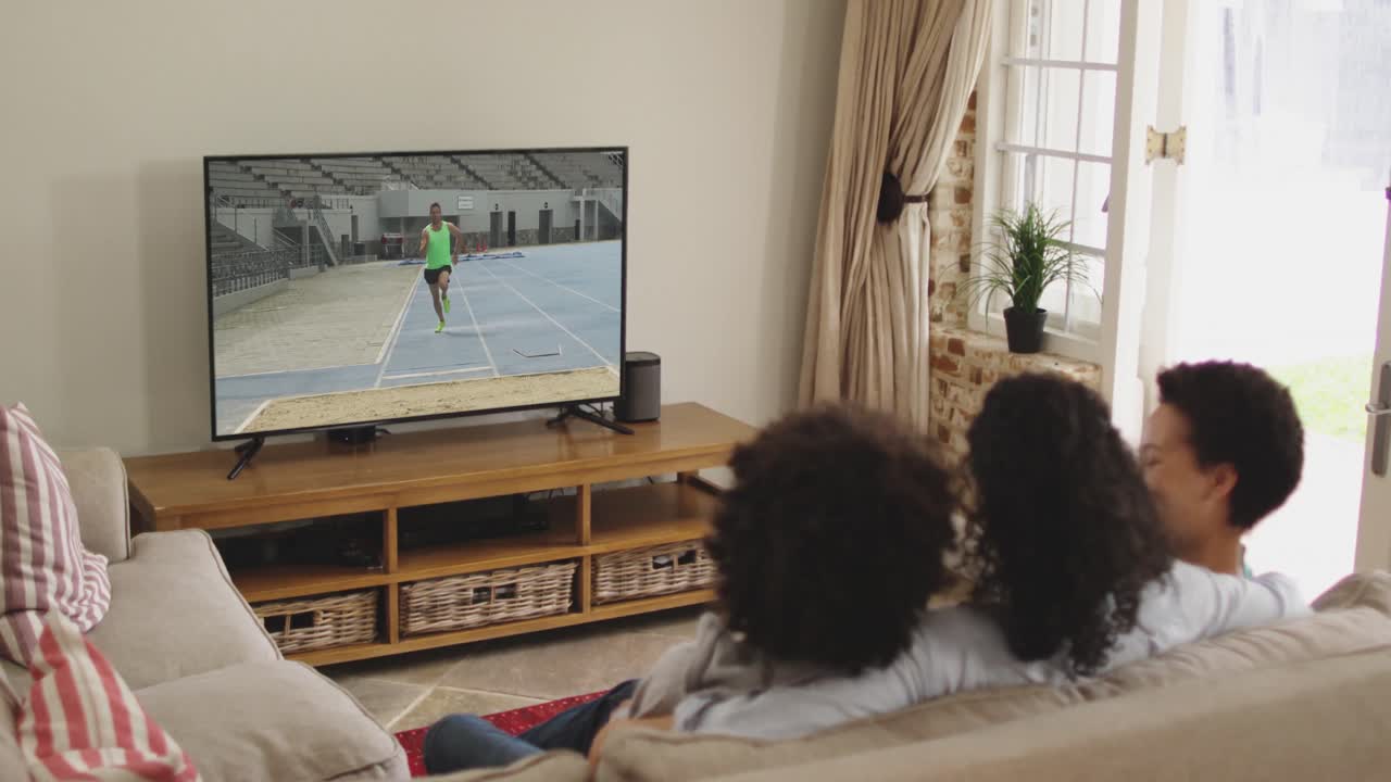 Composizione: famiglia felice seduta a casa insieme che guarda l'atletica del salto in lungo in TV.