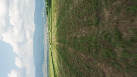 Vertical-video:-low-aerial-shot-over-harvested-farmland,-hay-bales-in-field