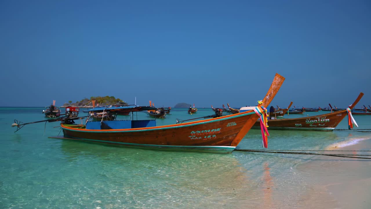 Famous and iconic Thai longtail boats on an empty sandy beach on the remote island Koh Lipe in Thailand, close to the Malaysian border. The water is turquoise and clear like in paradise.