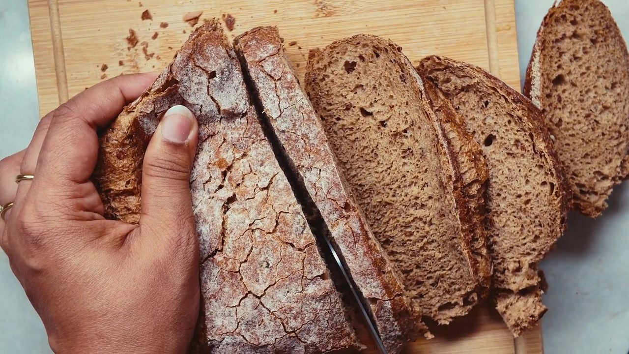 Person schneidet frisches handwerkliches Brot auf einem Holzbrett.