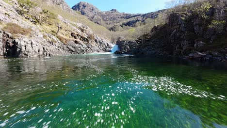 fpv drone flying above crystal clear water and rapids of river in sunny landscape of norway