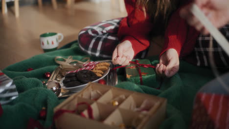 woman making ribbon bow on wrapped christmas gift