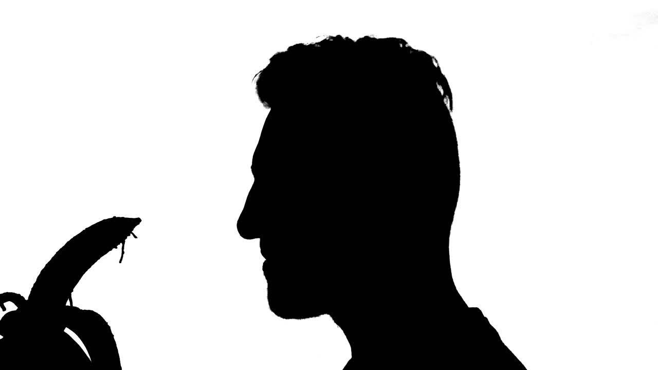 껍질을 벗기고 바나나를 먹는 젊은 남자, 흰색 배경에 검은 실루엣