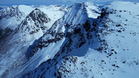 Slow-aerial-drone-flight-along-massive-snow-covered-mountains-lighting-by-sun-in-Norway,Europe---Beautiful-winter-scene-with-steep-wall-into-valley