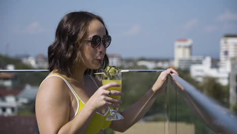 slow motion shot of a female in a bright bikini drinking her cocktail on a balcony