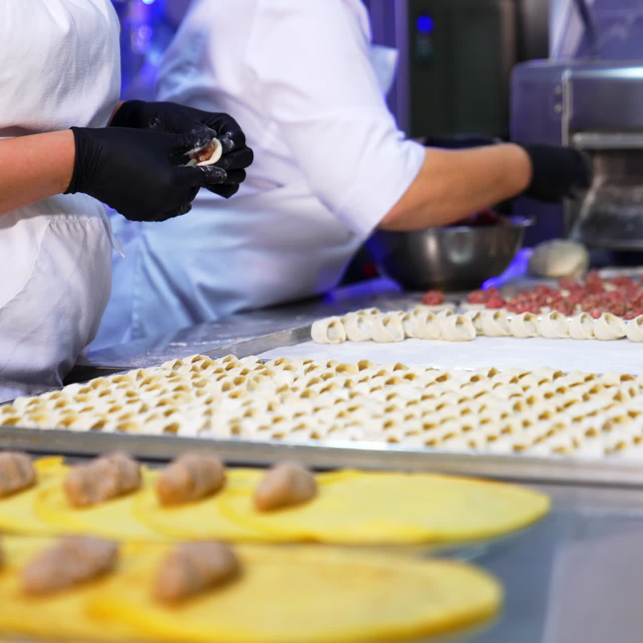 Workers at food factory make dumplings with minced meat. Freshly-made half-stuff products are laid on the trays on the table