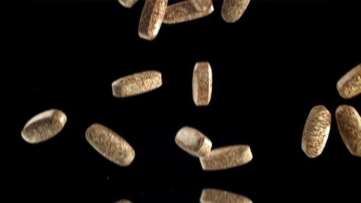 Brown Oval Pills Falling and Bouncing on Black Reflective Surface in Slow Motion