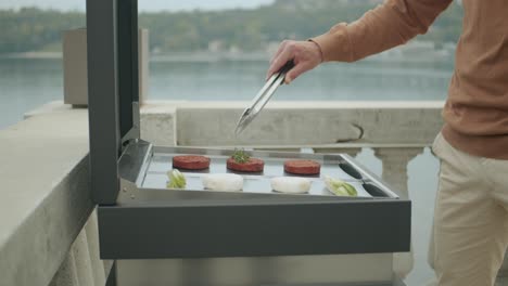 close up shot of man cooking outdoor on small barbecue in front of lake view