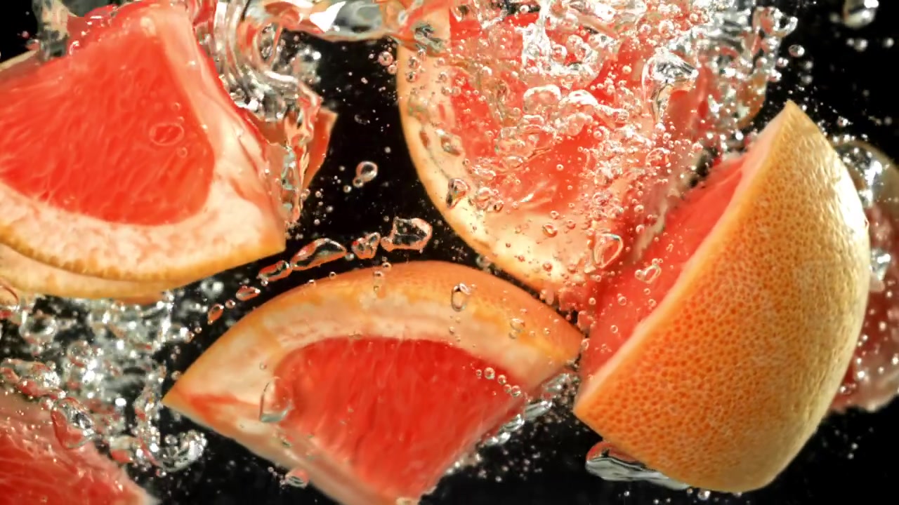 Frische Grapefruitscheiben spritzen in Zeitlupe ins Wasser