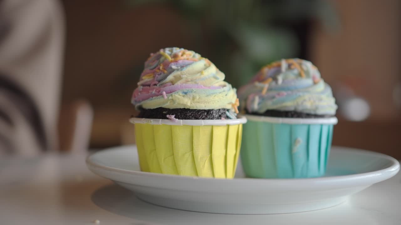 Mão pegando um cupcake colorido de um prato