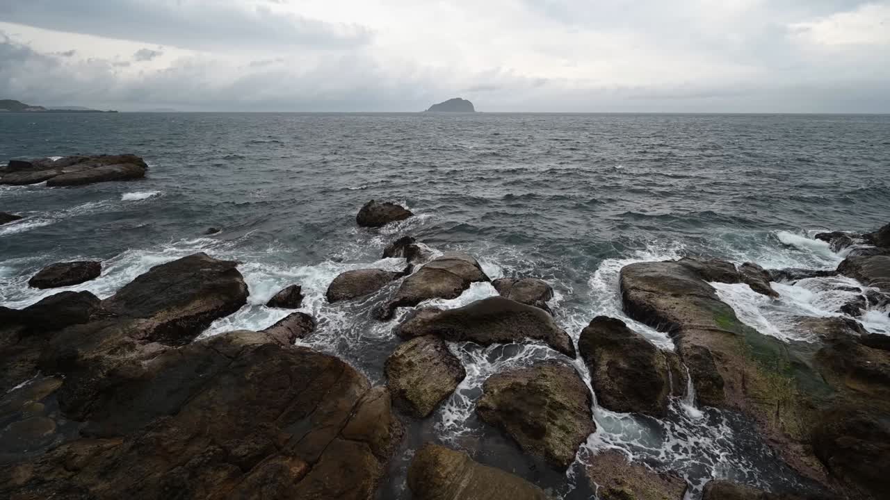 Giornata ventosa sul litorale, grandi onde si infrangevano sugli scogli, il cielo era molto nuvoloso e una piccola isola in mezzo all'oceano, a Keelung, Taiwan.