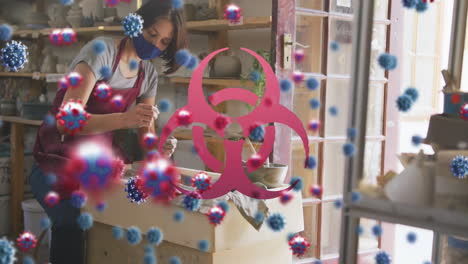 animation of virus cells and biohazard symbol over caucasian woman with face mask forming pottery