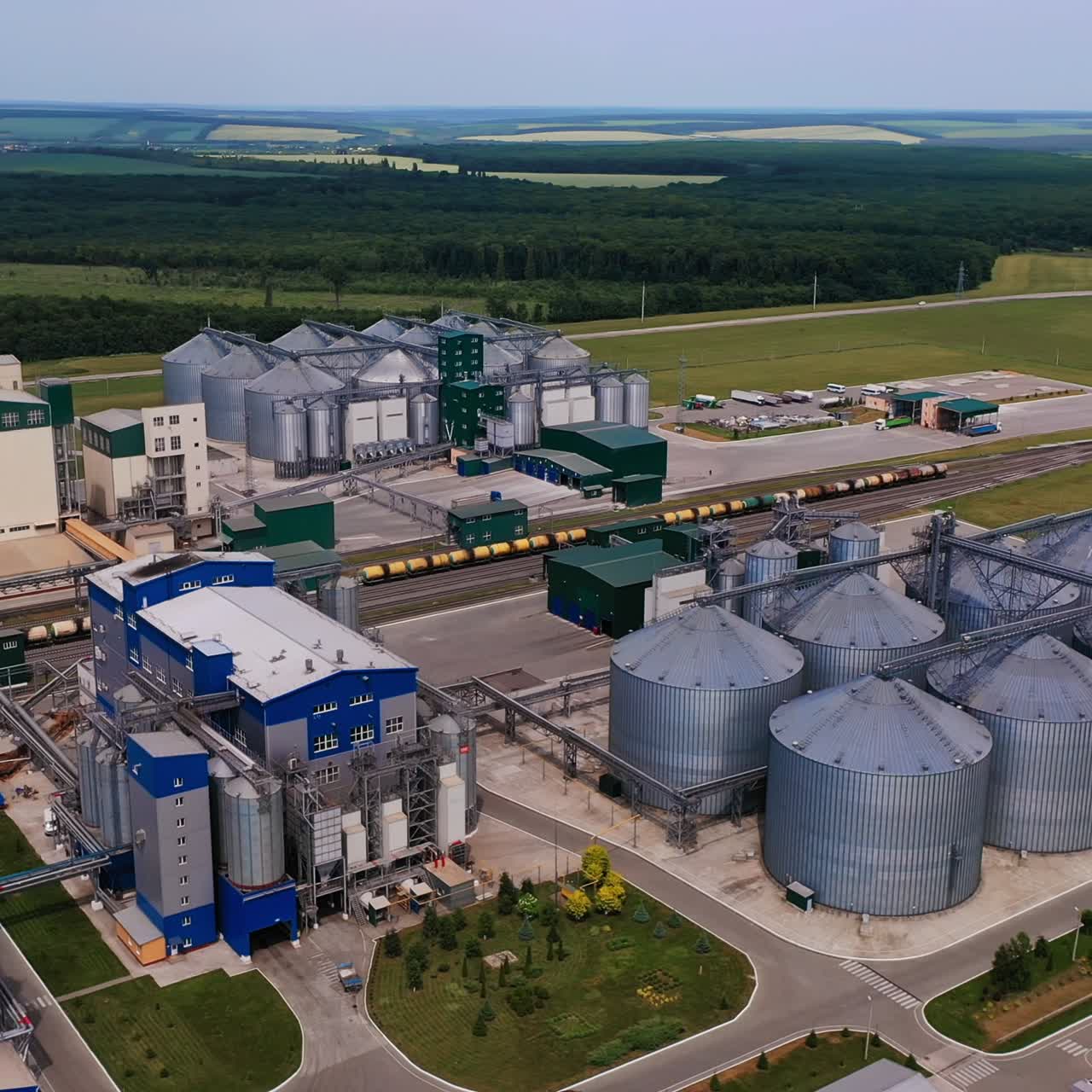 Modern technological plant for storage and processing grain crops. Well-kept industrial territory divided by railways with cargo trains. Beautiful nature landscape background