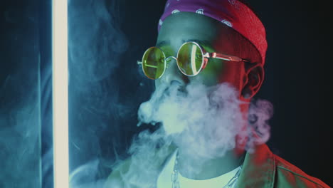 stylish man exhaling smoke with neon lights