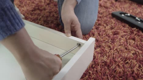 man tightens a screw on a desk drawer, close-up of his hand